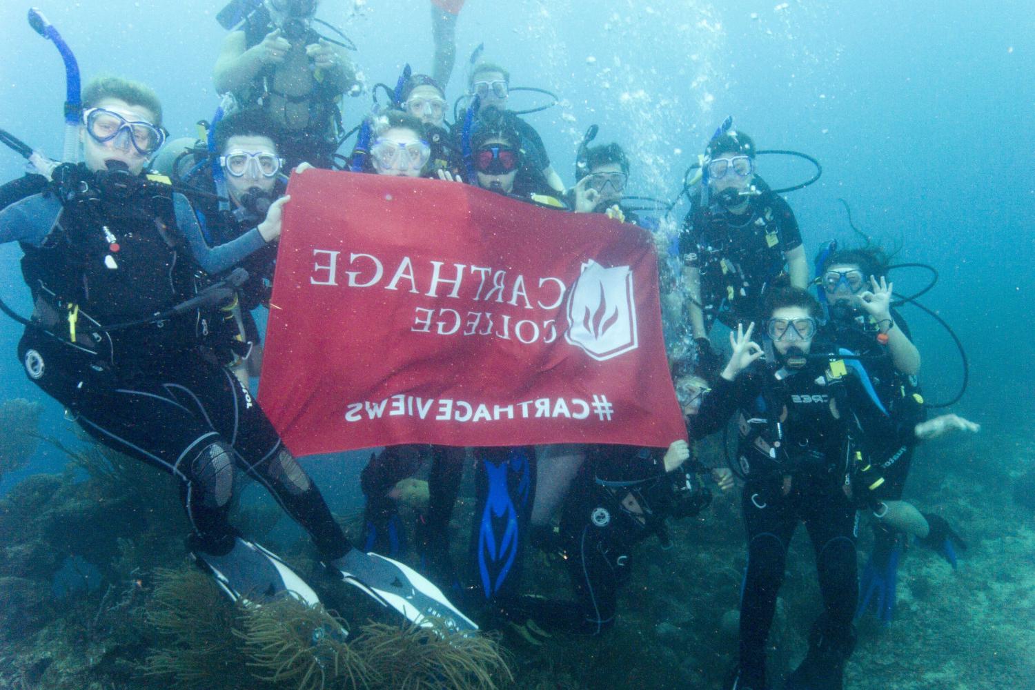 Students hold a Carthage flag while scuba diving on the j项 study tour to Honduras.